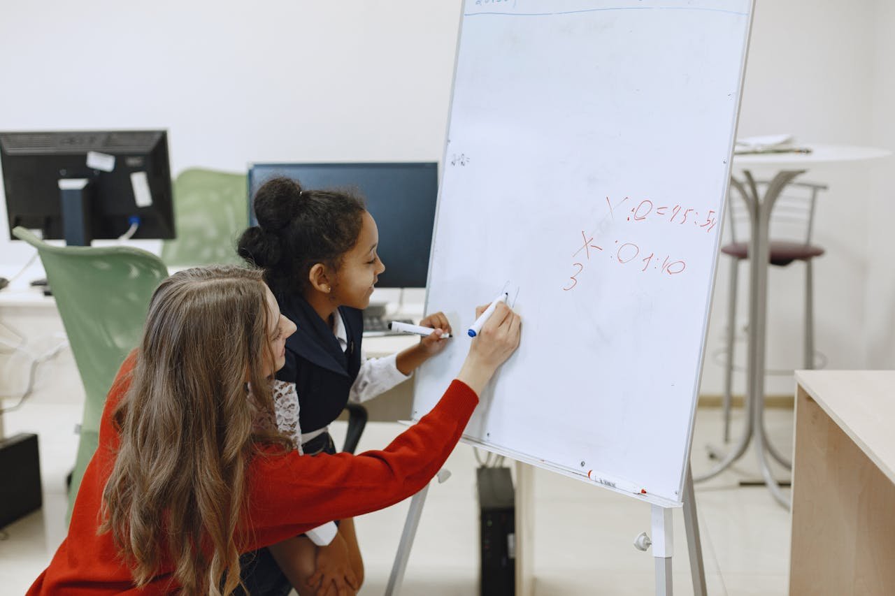 gallery-1 A teacher helps a student with math on a whiteboard in a classroom setting.