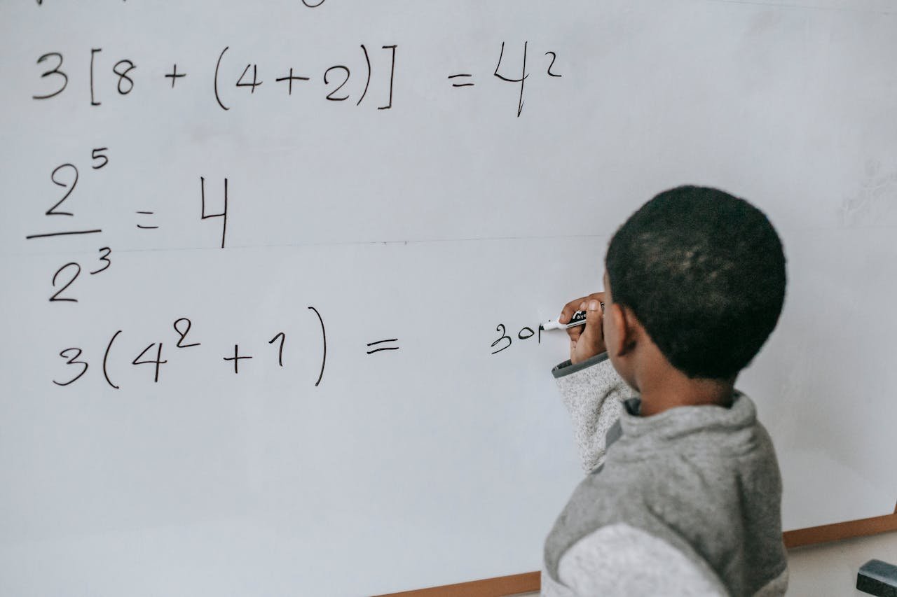 gallery-2 Back view of anonymous African American boy writing on whiteboard while doing sums on mathematics class