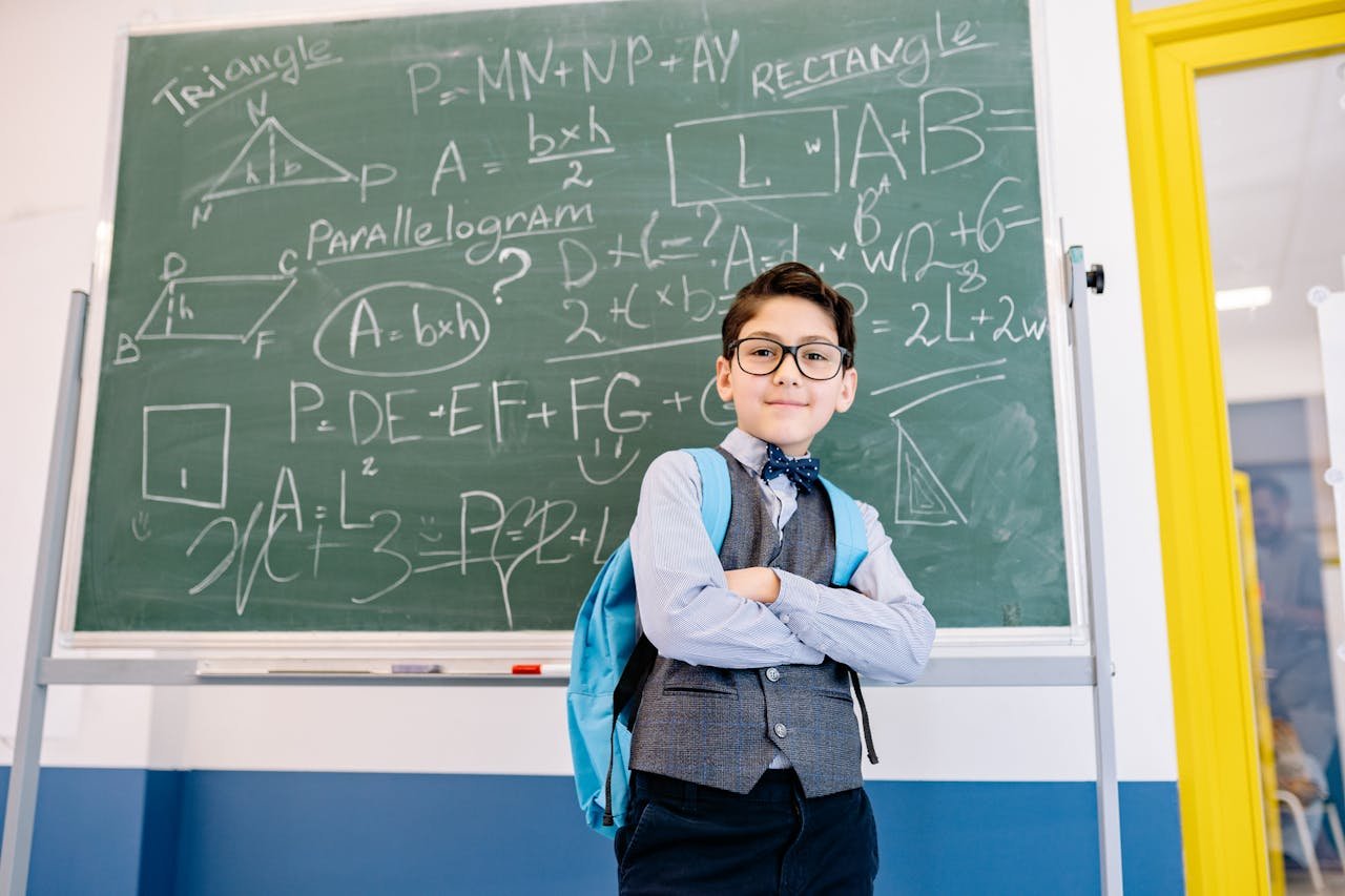 hero-img-02 A young student stands confidently with arms crossed in front of a chalkboard filled with math equations.
