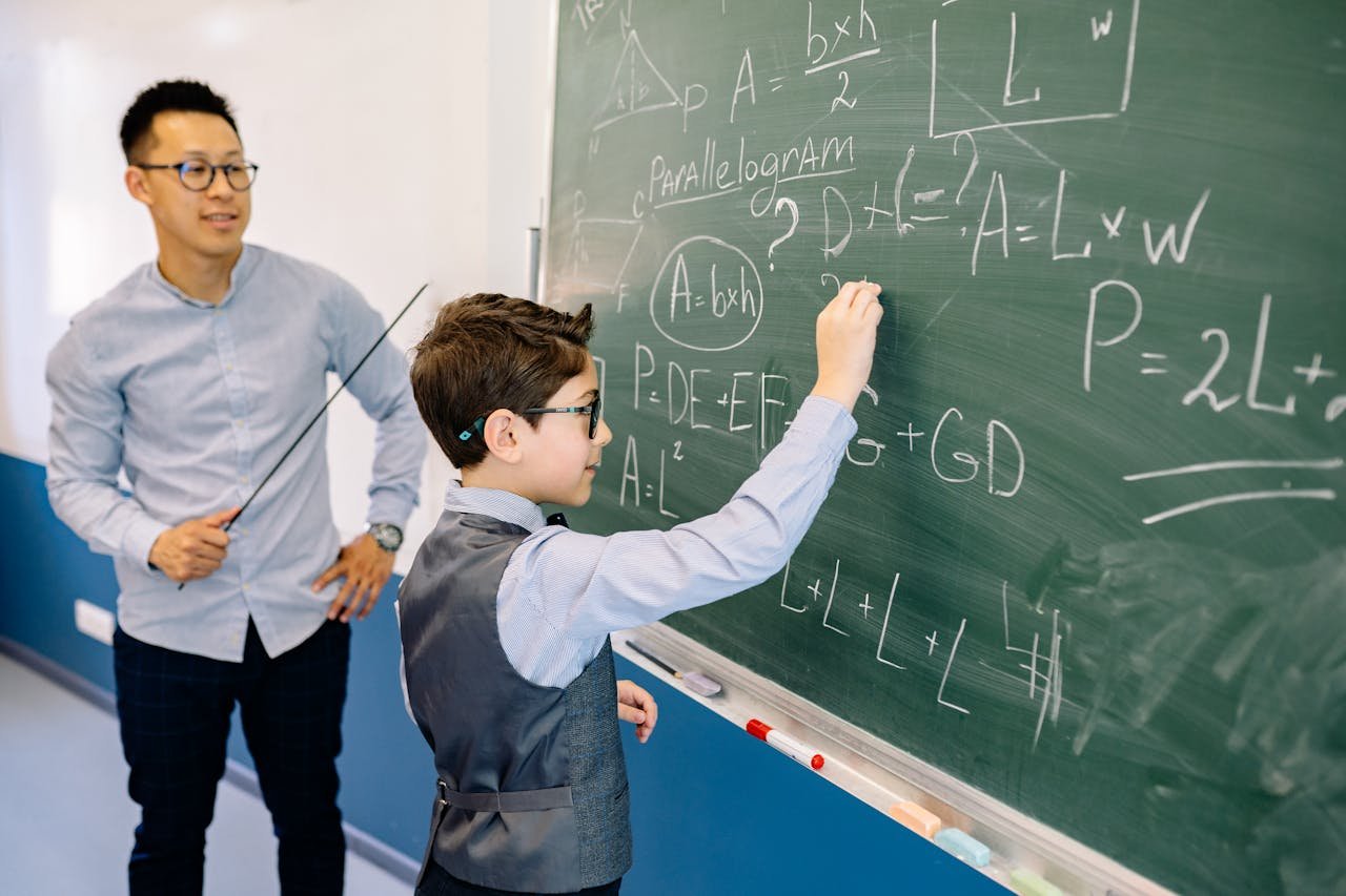services-02 A teacher guides a student solving math equations on a classroom chalkboard.