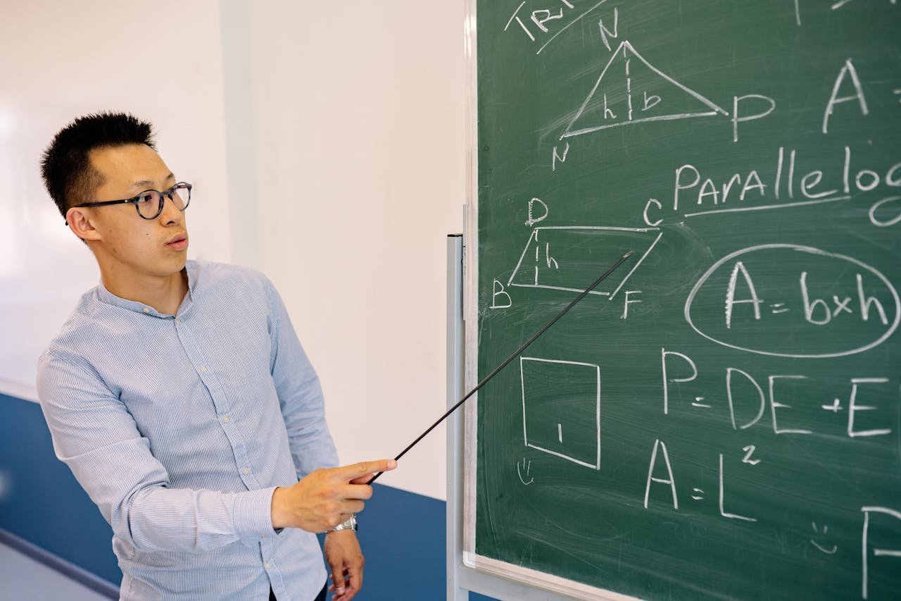 hero-img-01 Math teacher demonstrating equations on the blackboard in classroom setting.